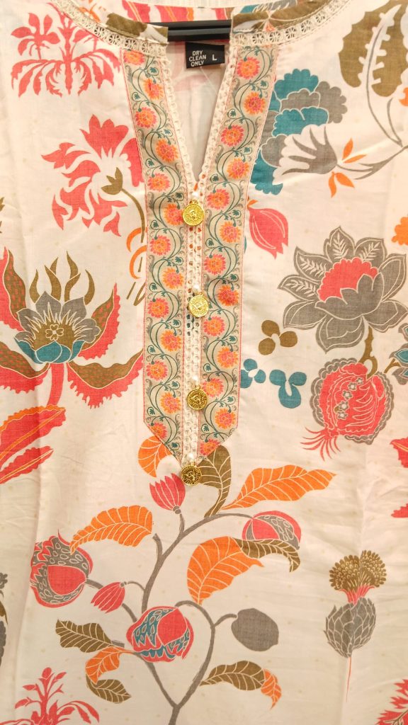 Close-up of a cream-colored floral printed kurta with a decorative embroidered neckline and gold buttons.